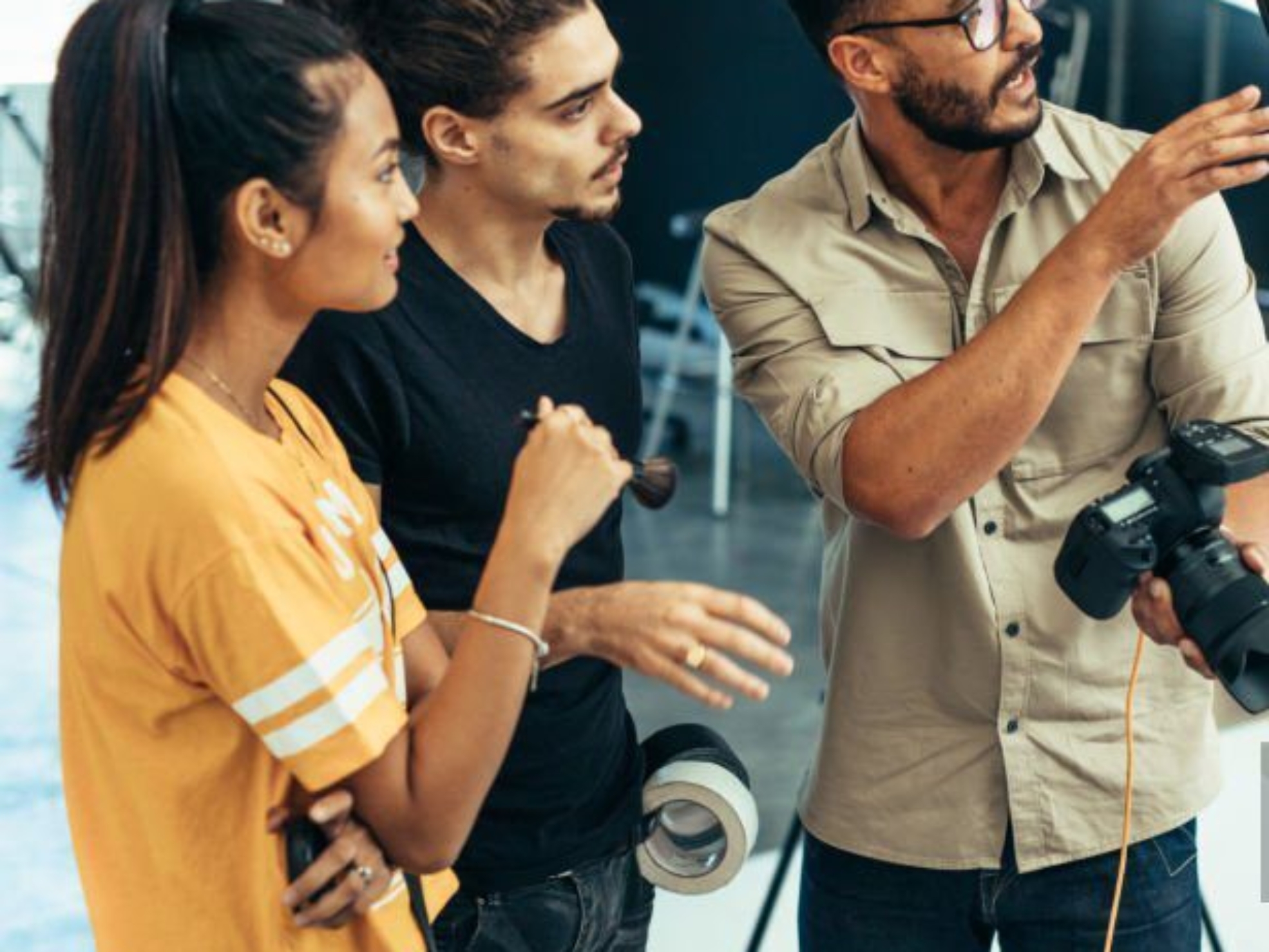 Photographer explaining about the shot to his team in the studio. Photographer talking to his assistants holding a camera during a photo shoot.